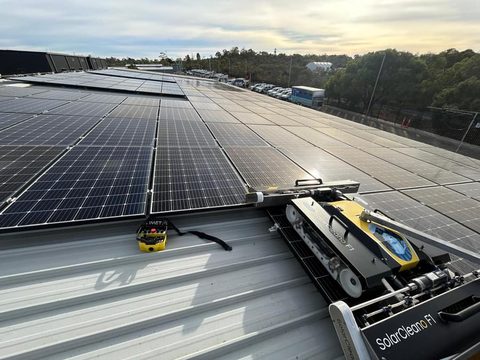 Purified Group technician operating a rooftop solar panel cleaning robot on a Perth commercial building at dusk