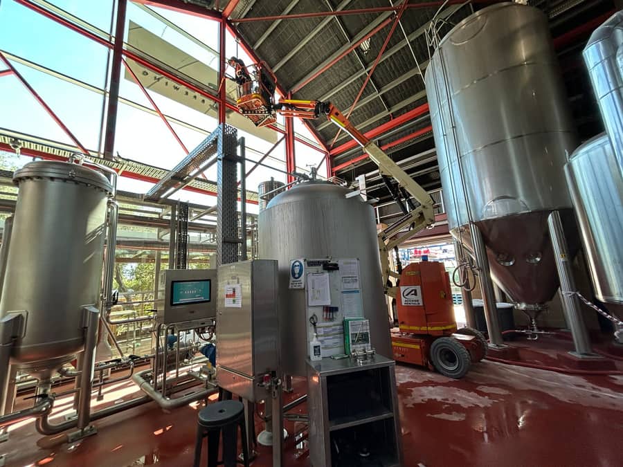 High-level cleaning inside a commercial brewery, technician working from a boom lift among steel tanks, Purified Group Perth