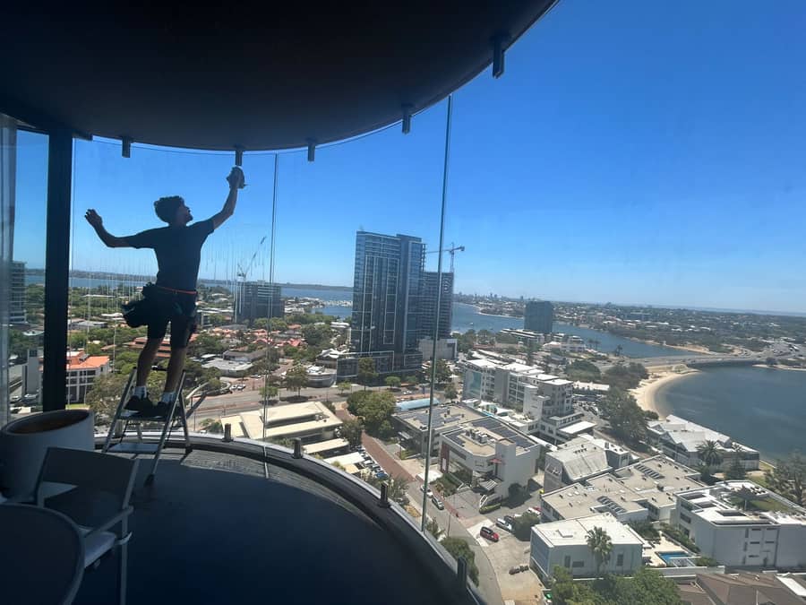 Technician cleaning high-rise apartment windows from a cherry picker overlooking the Perth CBD and Swan River