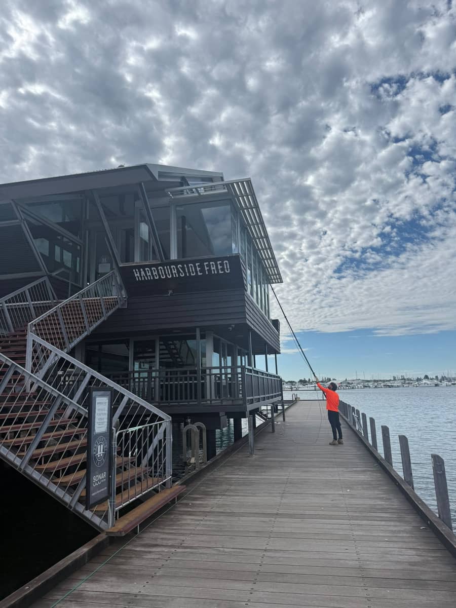 Technician pole-cleaning windows at a waterfront restaurant on Perth's coast