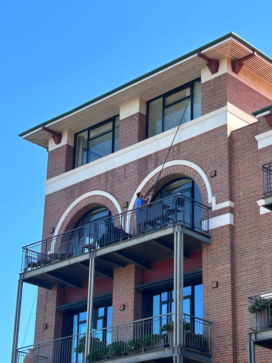 Technician pole-cleaning upper-storey windows on a brick apartment building, Perth