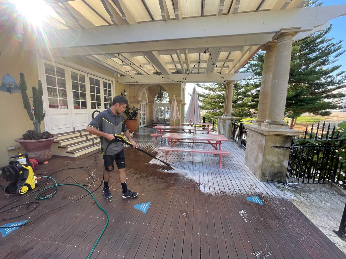 Purified Group technician pressure-washing a commercial driveway and forecourt in Perth