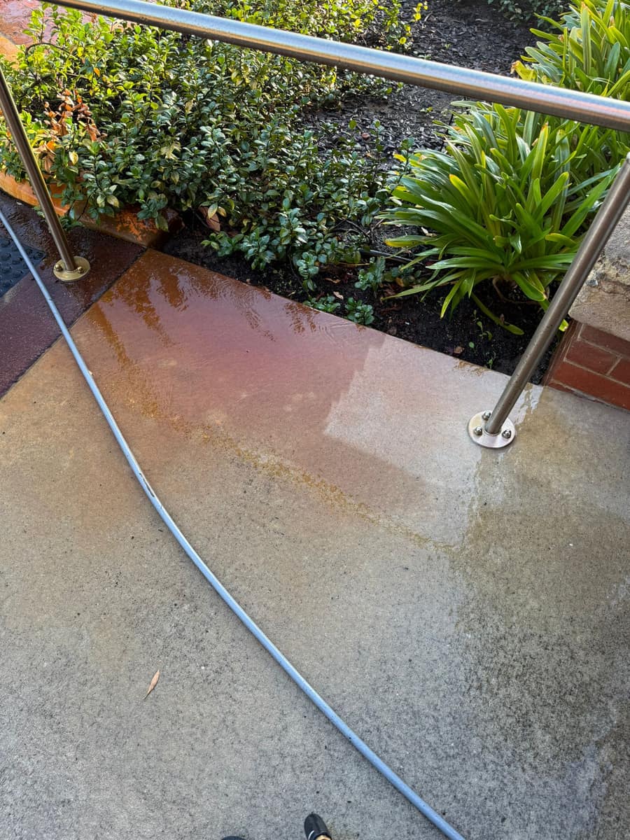 Pressure-cleaned paved walkway mid-pass, spray and runoff visible, Perth