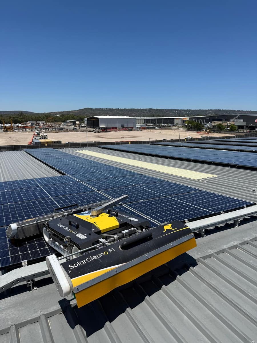 Solar panel cleaning robot on a commercial rooftop, logistics precinct in the background, Perth