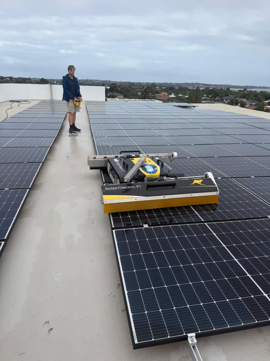 Technician cleaning commercial solar panels with the Perth skyline in the background