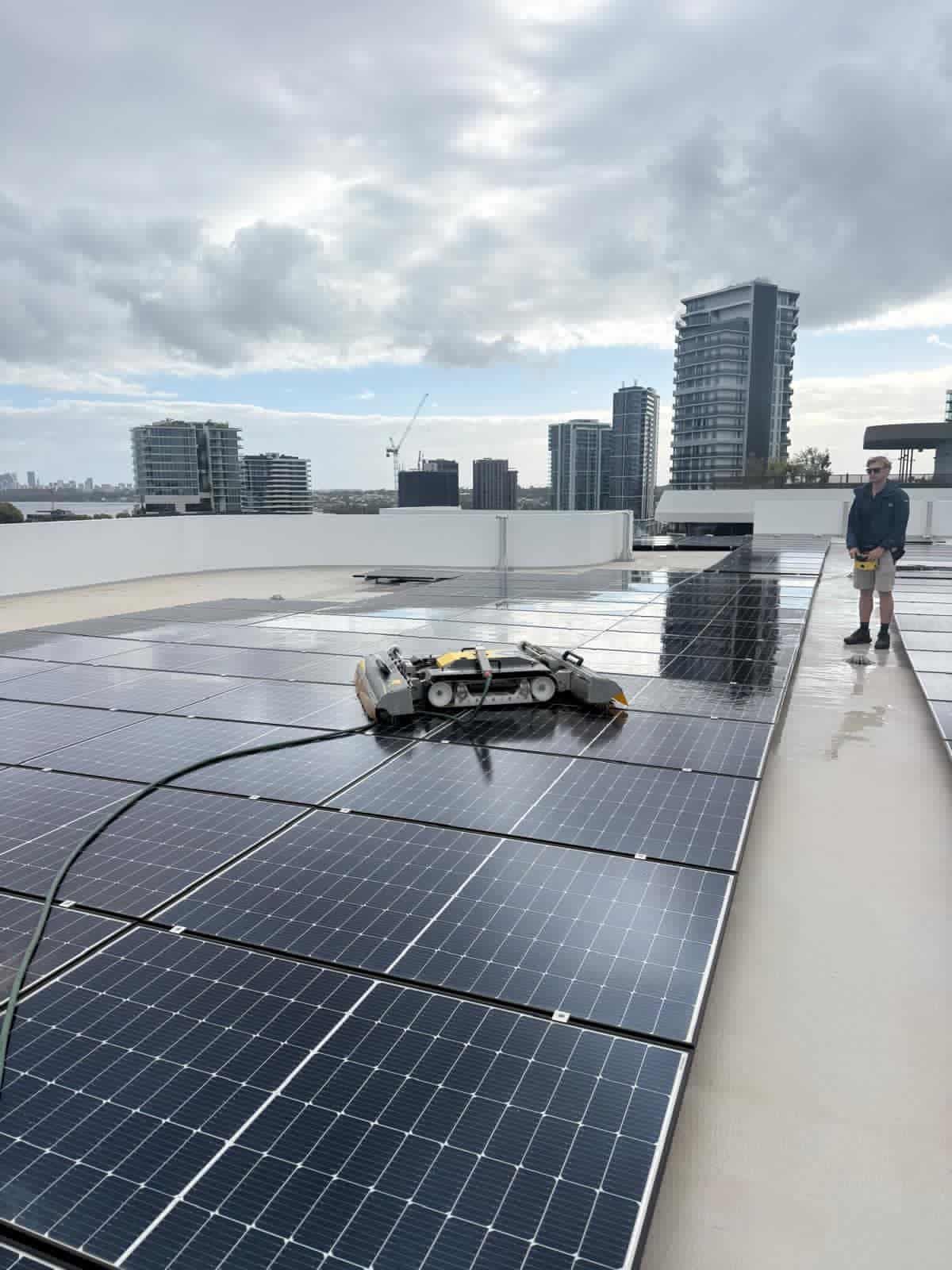 Technician with a robotic solar panel cleaner, apartment towers and river in the background, Perth