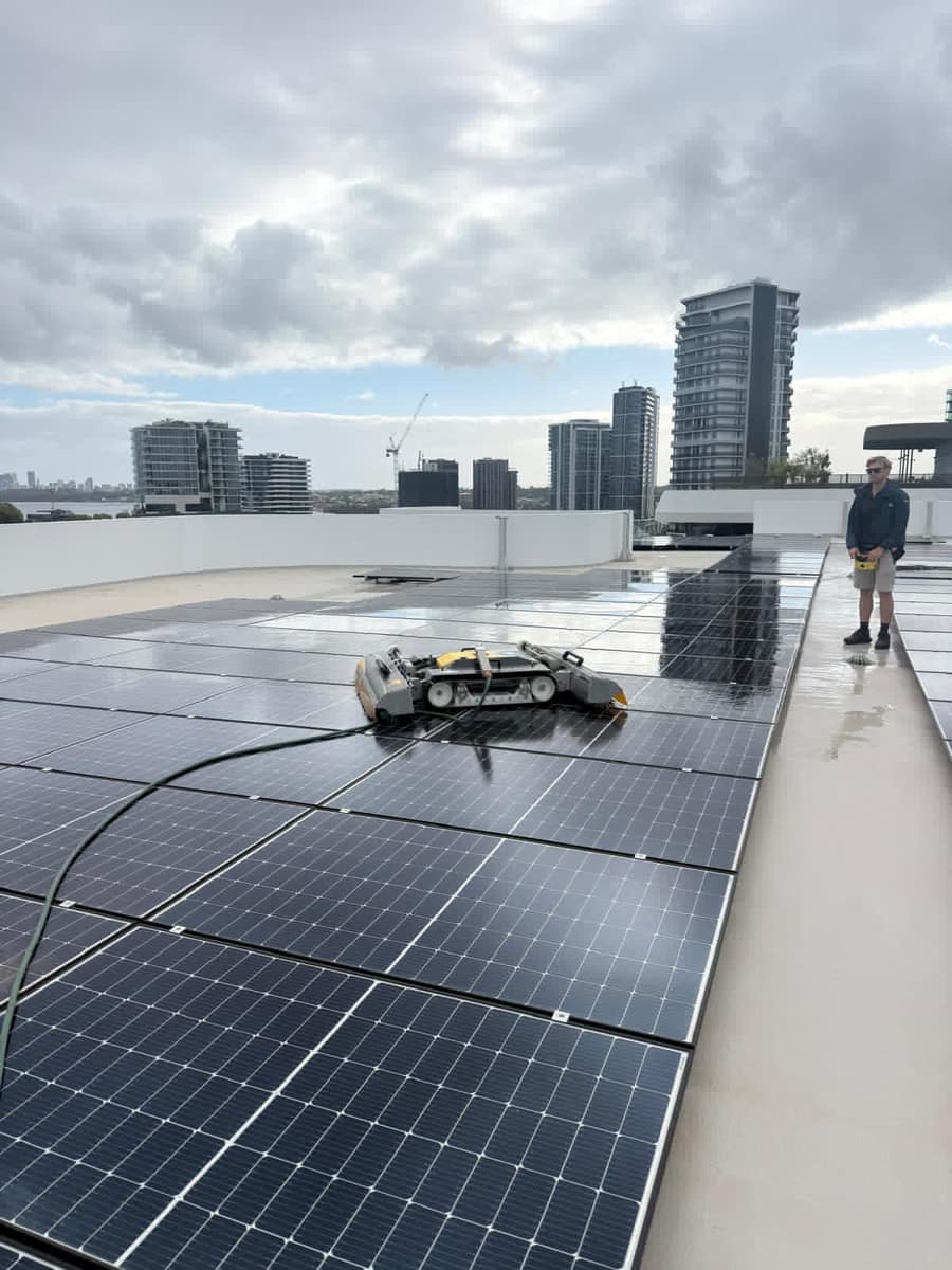Technician with a robotic solar panel cleaner, apartment towers and river in the background, Perth