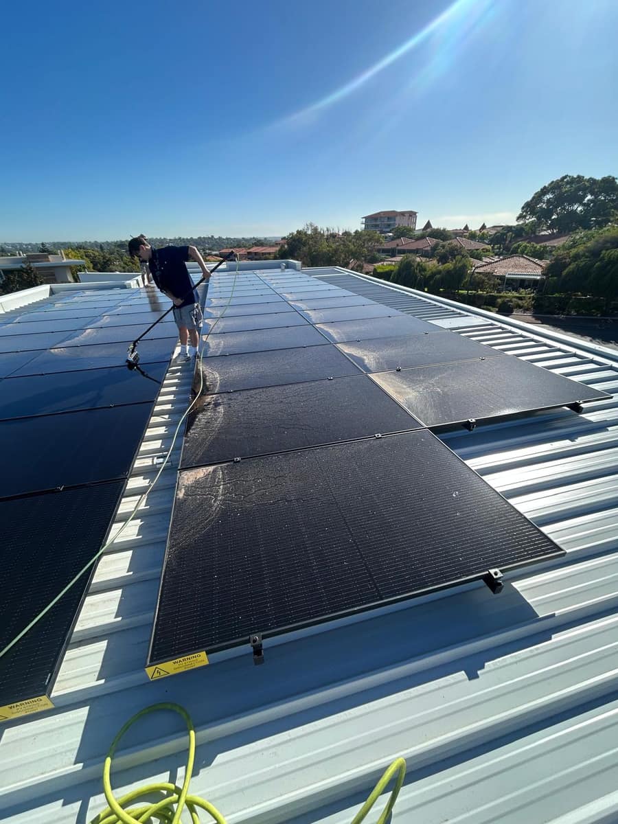 Technician hand-cleaning residential solar panels with a pole and hose, Perth
