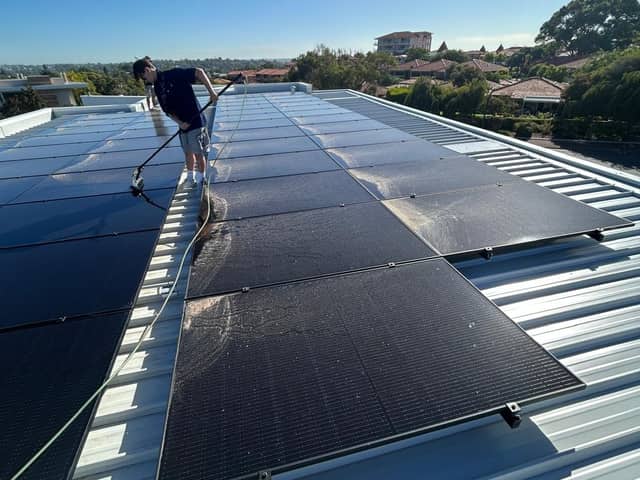 Purified Group technician cleaning a residential solar array with a water-fed pole, Perth suburban rooftops behind