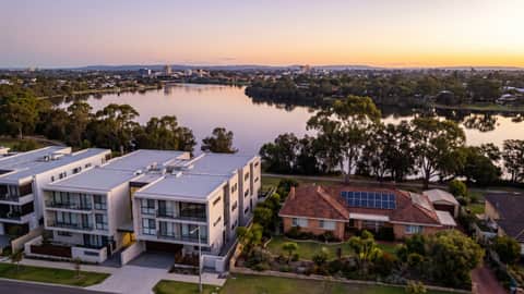 A Perth riverside suburb under jacaranda and gum trees, a home with solar panels visible, Como