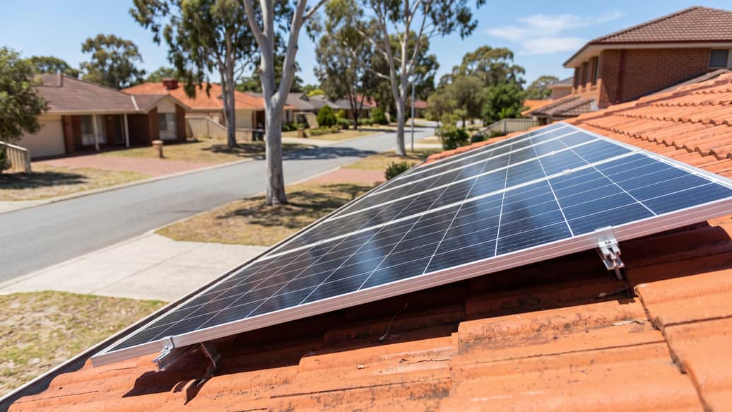 Solar panels on a terracotta tile roof overlooking a quiet Perth street lined with gum trees, Murdoch