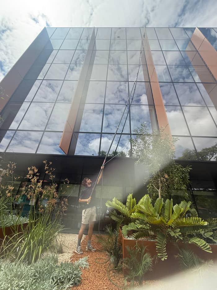 Technician on an extension pole cleaning a commercial glass curtain wall, Perth