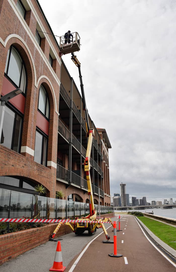 Technician on a cherry-picker cleaning windows high on a brick commercial building, Perth city skyline behind