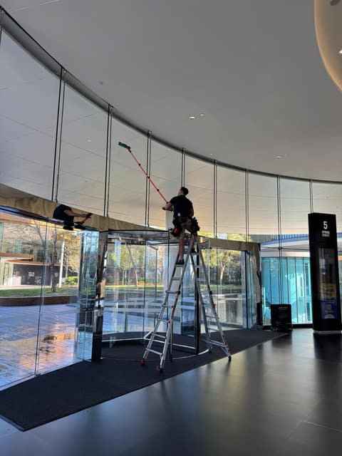 Cleaner on a ladder with a water-fed pole cleaning a building atrium ceiling, Perth