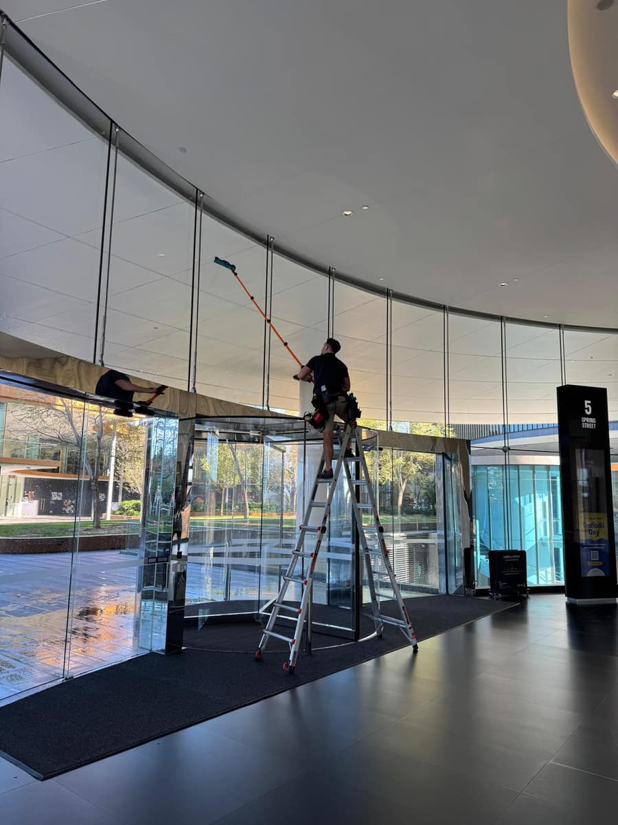 Cleaner on a ladder with a water-fed pole cleaning a building atrium ceiling, Perth