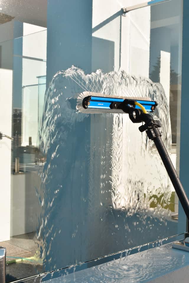 Close-up of a water-fed pole brush cleaning glass with visible water spray