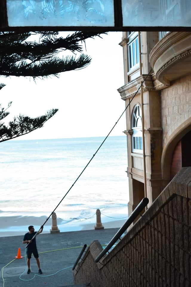 Technician using a water-fed pole to clean the salt-hazed windows of a private coastal Perth home